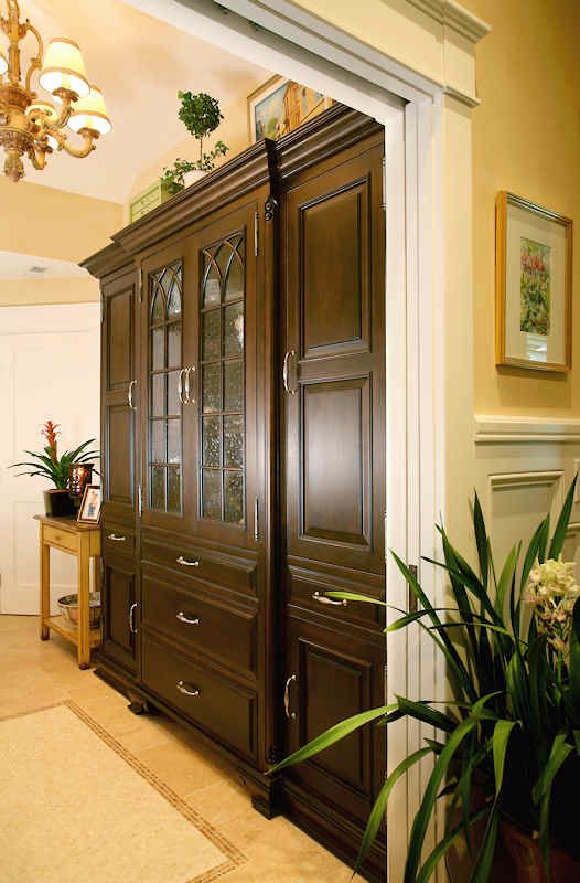 Dark wood cabinet with glass door, drawers, and cabinet doors in an entryway; gold walls.