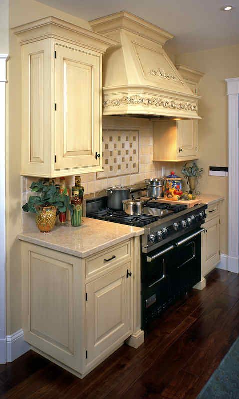 Cream-colored kitchen cabinets and range hood. Dark range, tile backsplash, countertop, and wood floor.