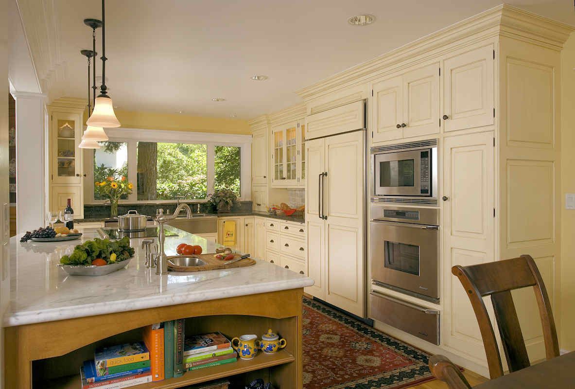 Cream-colored kitchen with island and stainless steel appliances. A large window offers a view of greenery.