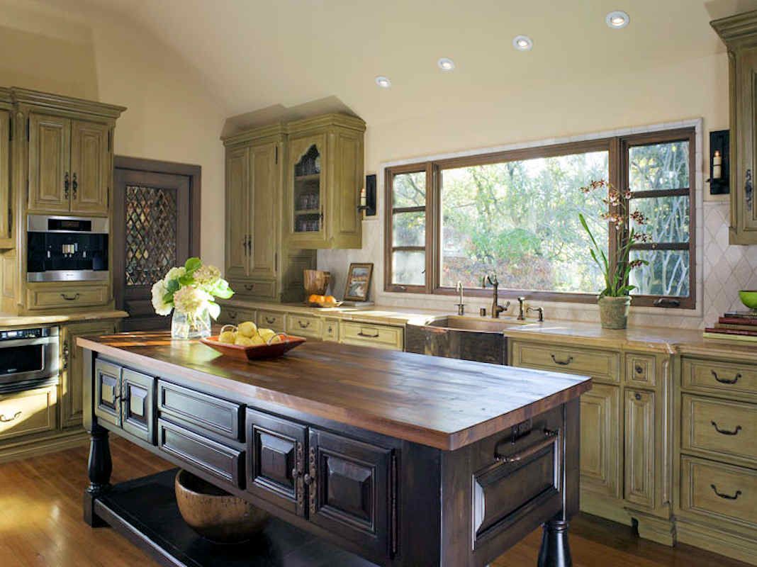 Kitchen with green cabinetry, dark wooden island, and a large window.