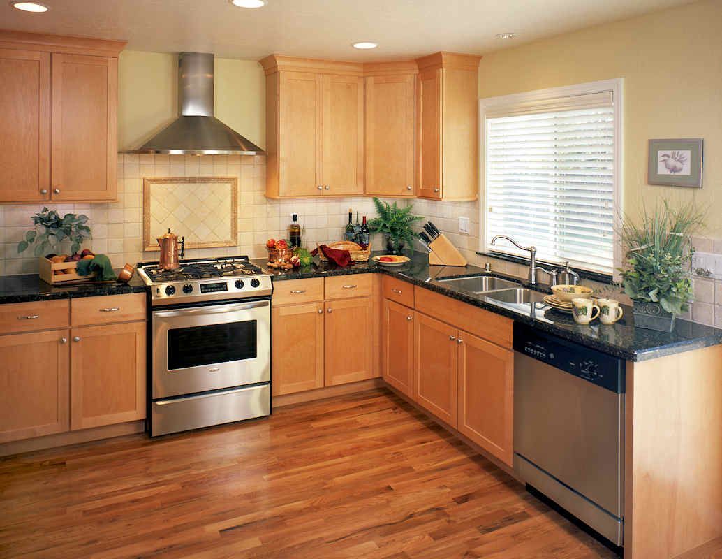 Kitchen with light wood cabinets, stainless steel appliances, and black countertops.