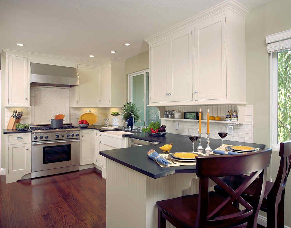 Kitchen with white cabinets, dark countertops, stainless steel appliances, and wooden flooring.