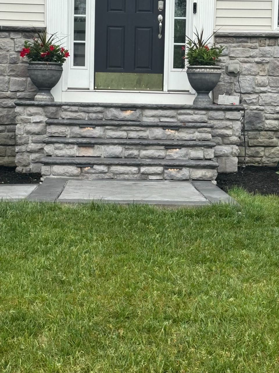 Stone steps leading to a house entrance, with potted flowers and green grass.