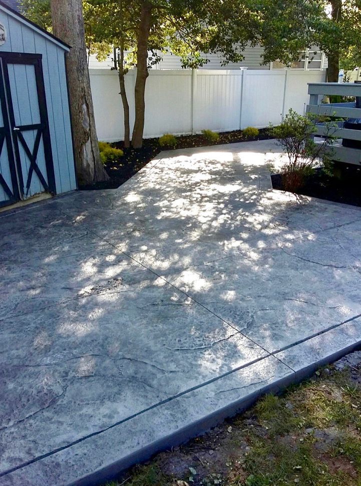 Concrete patio with a shed, fence, and sunlight.