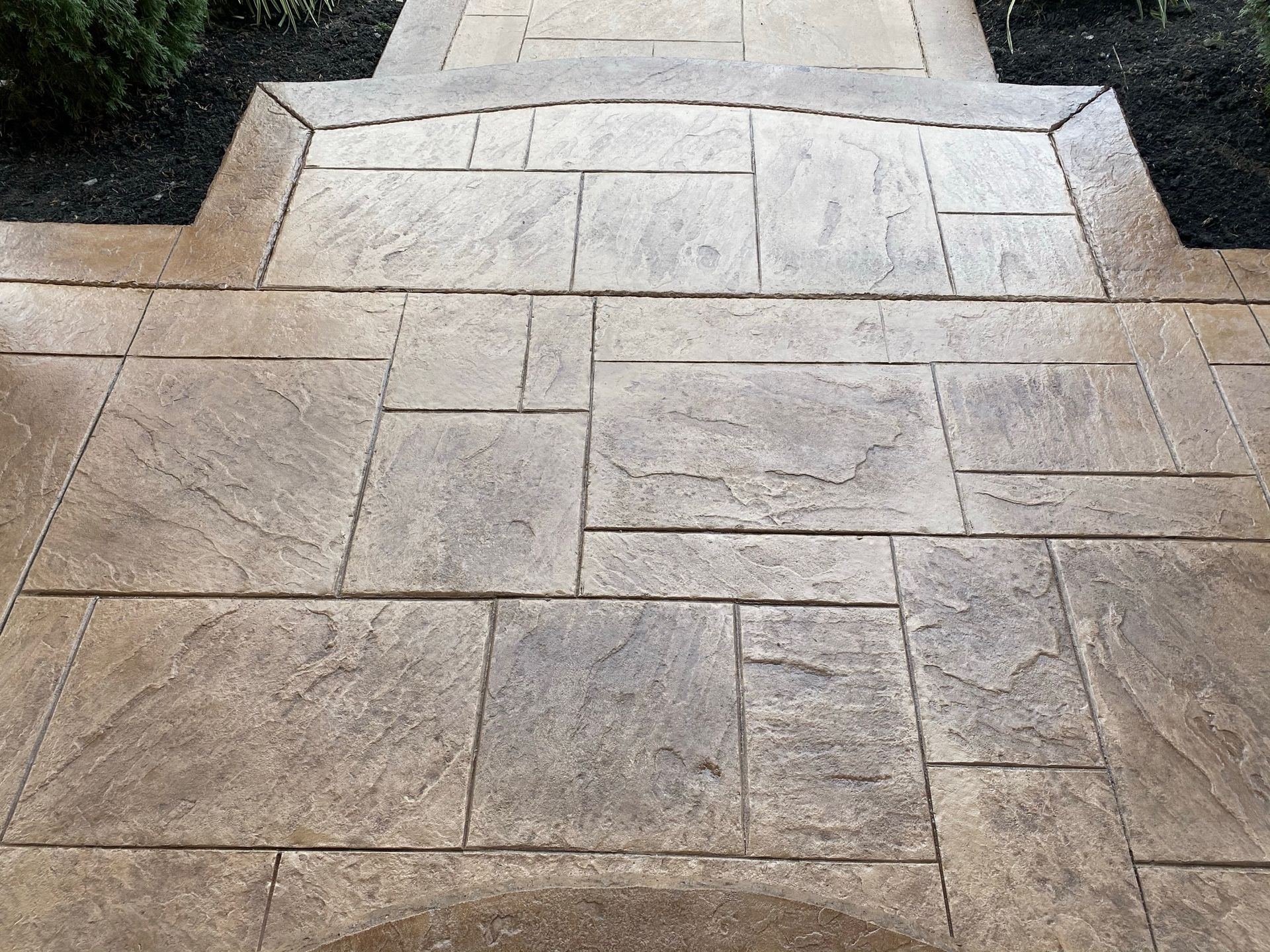 Beige stamped concrete walkway with a curved edge and dark mulch border.
