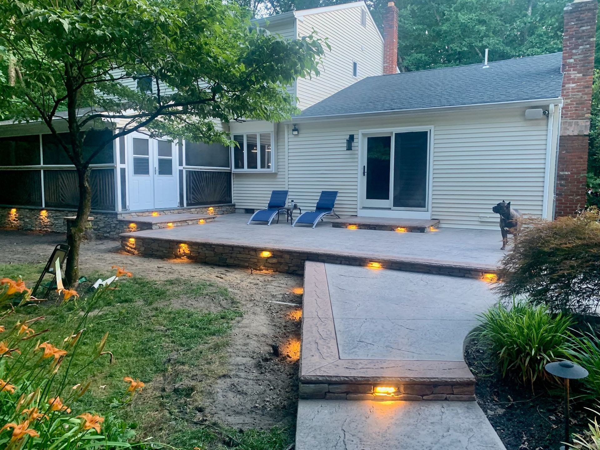 Backyard patio with steps, landscape lighting, and blue lounge chairs.
