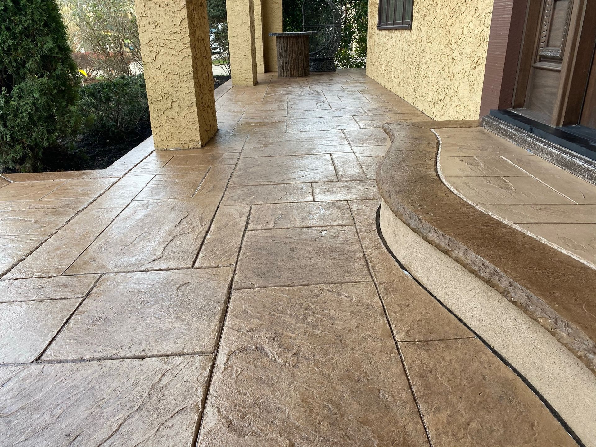 Stamped concrete porch with beige and brown tones, leading to a house entrance.