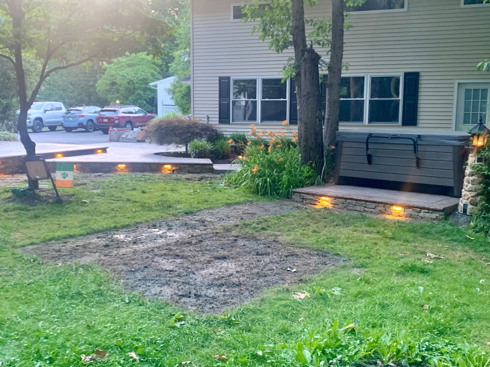 A house exterior with a grassy lawn, concrete steps, a bench, and parked cars. Dusk lighting.