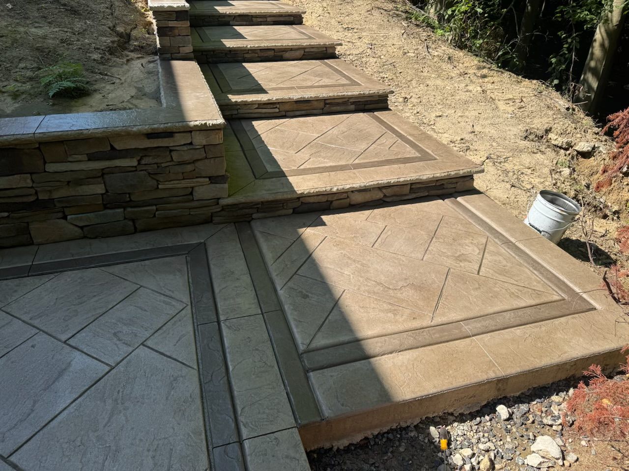 Concrete steps with decorative stone edges, ascending a sloped yard.
