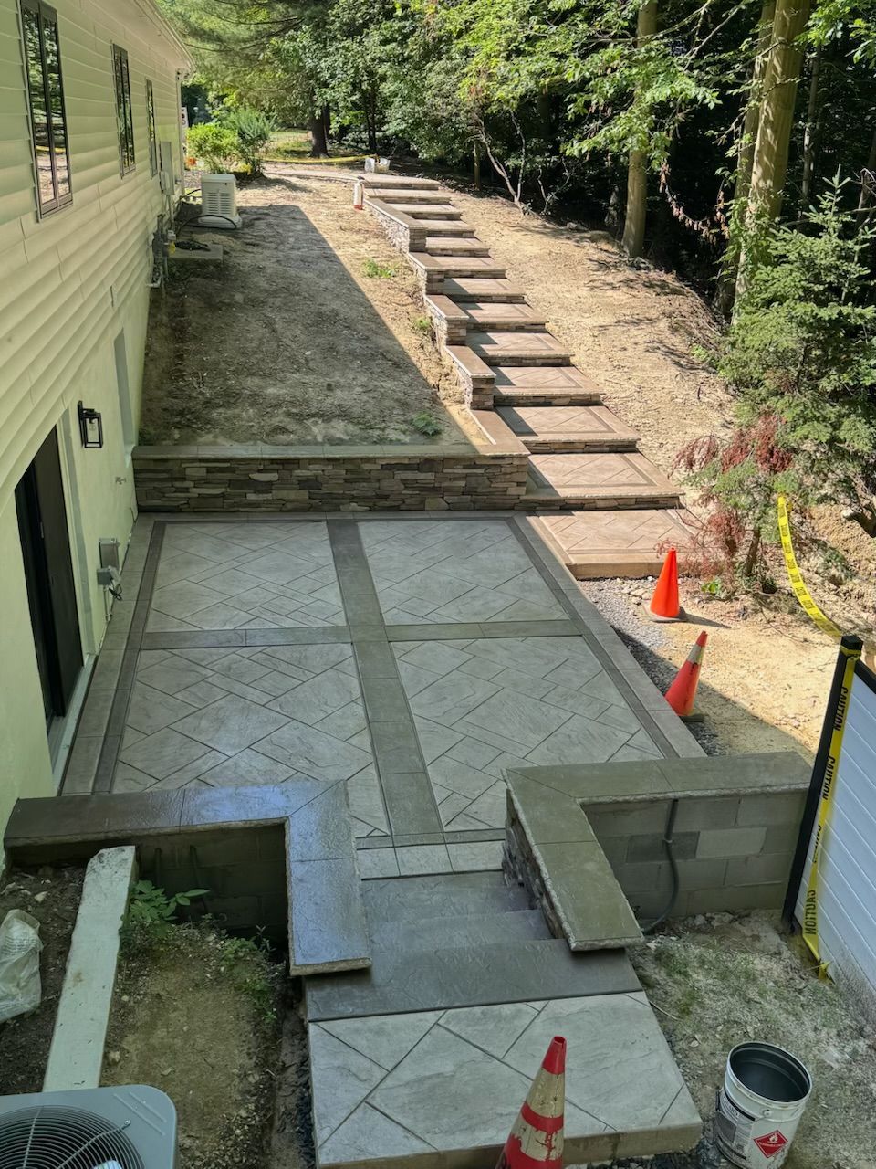 A paved patio with stairs leading up a sloped yard next to a house.
