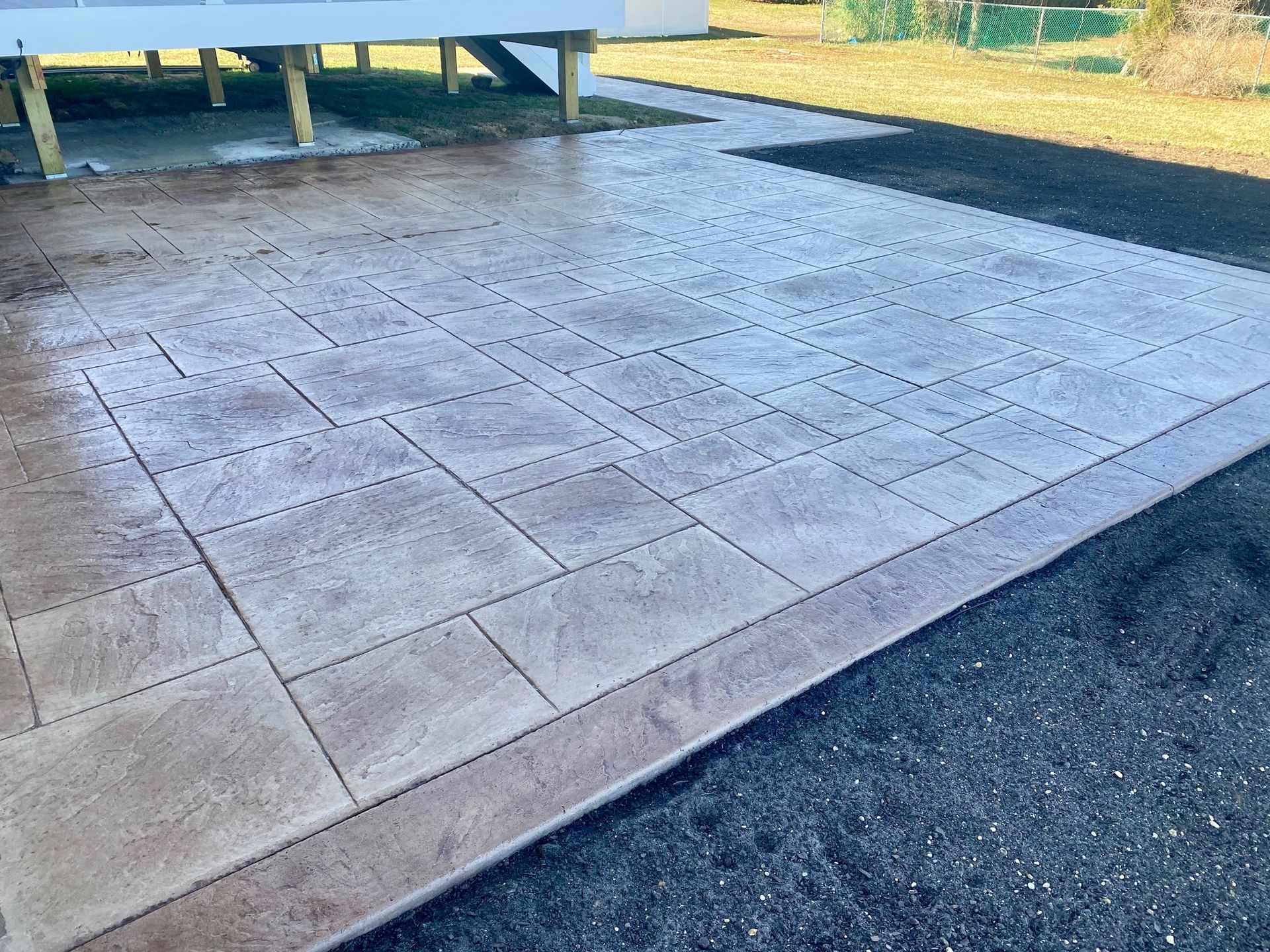 Stamped concrete patio with brown border next to a grassy area and house deck.