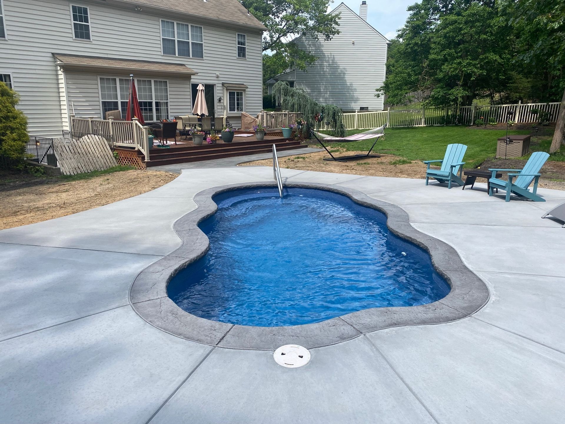 Swimming pool with concrete patio, Adirondack chairs, and house in background.