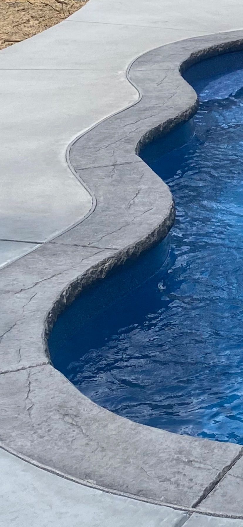 A wavy-edged swimming pool with a gray concrete border and blue water.