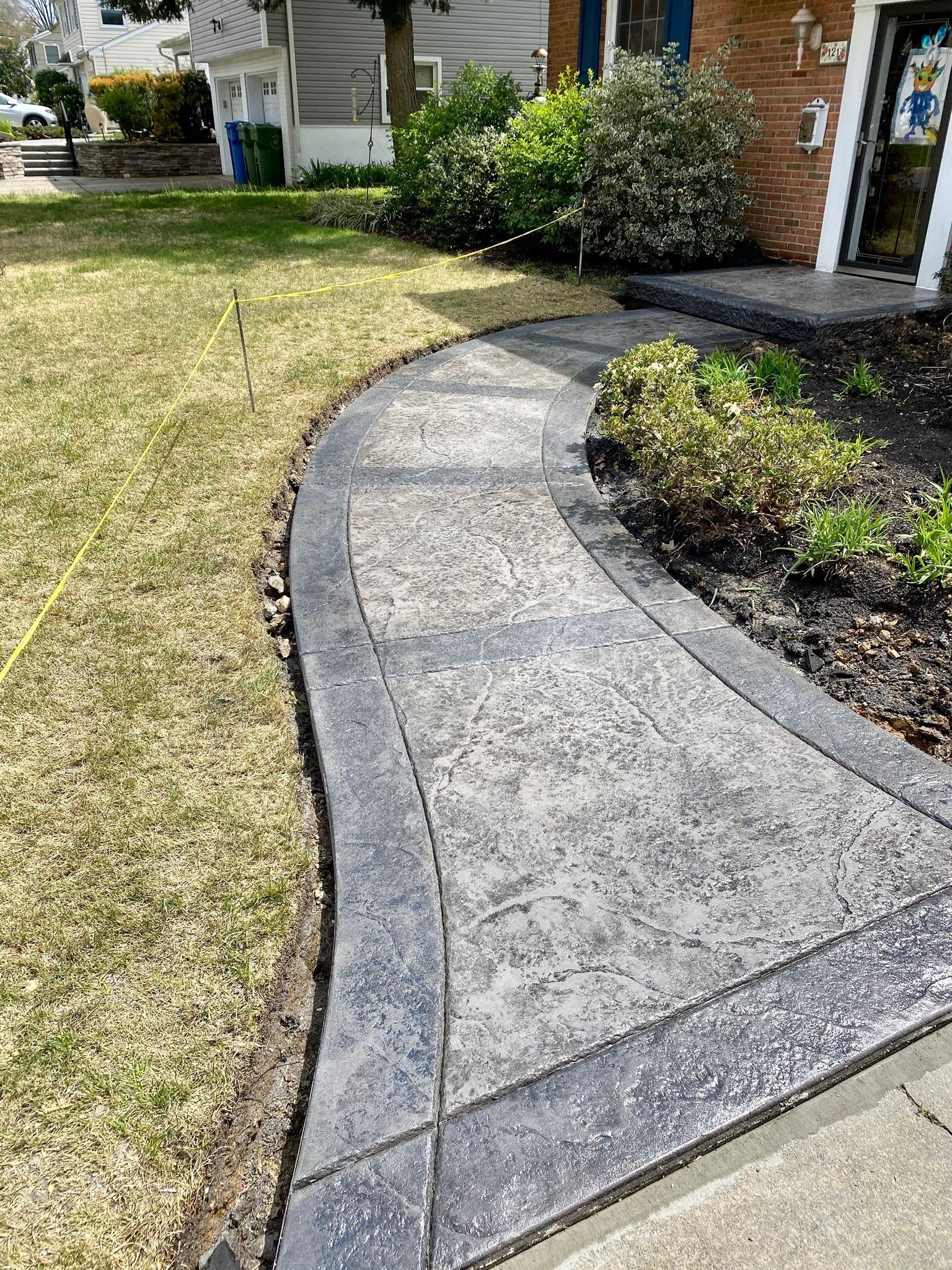 Concrete walkway with dark border curves from lawn to house entrance.