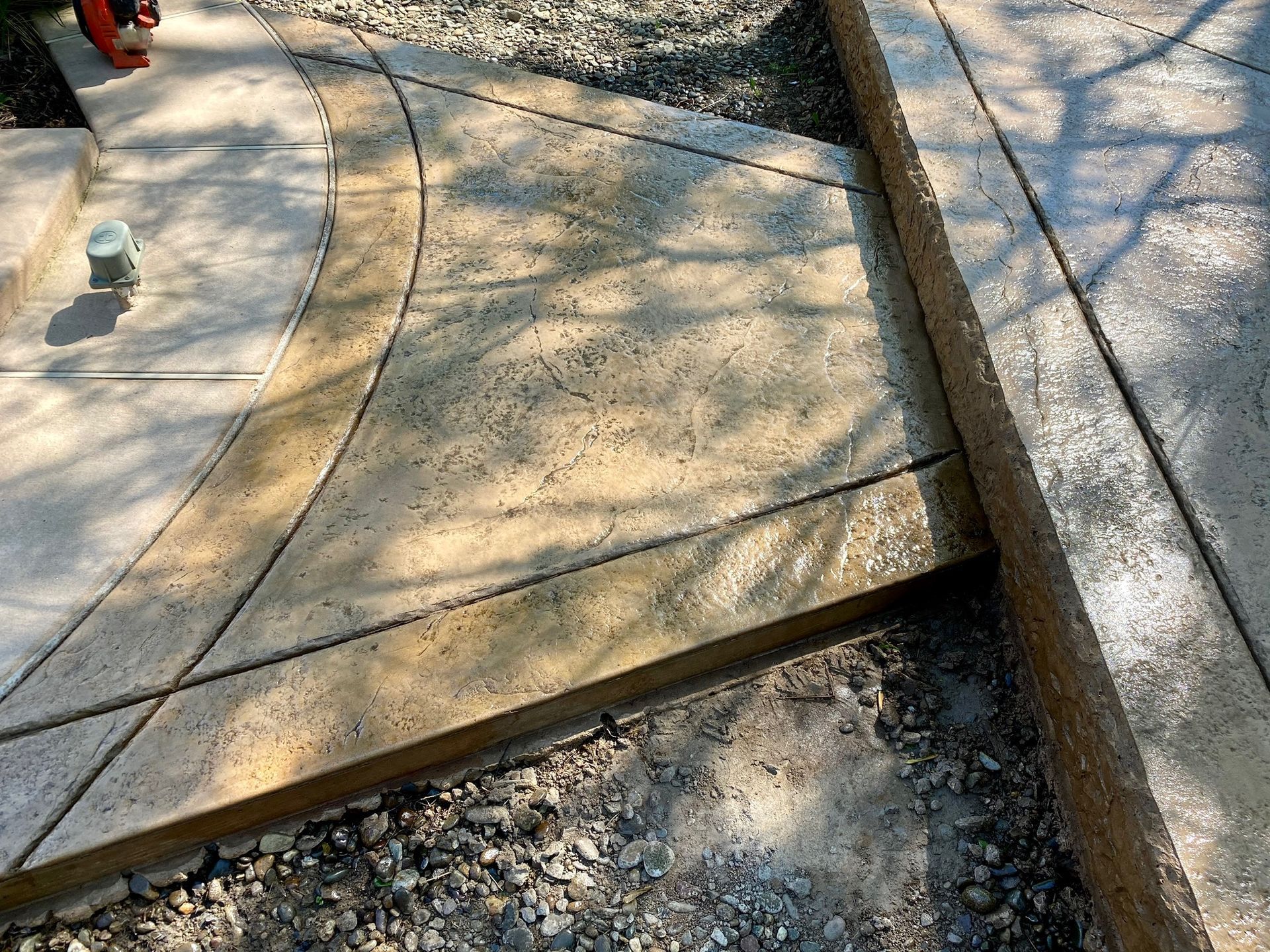 Concrete patio with curved sections and angular cuts, surrounded by gravel and a wooden border.