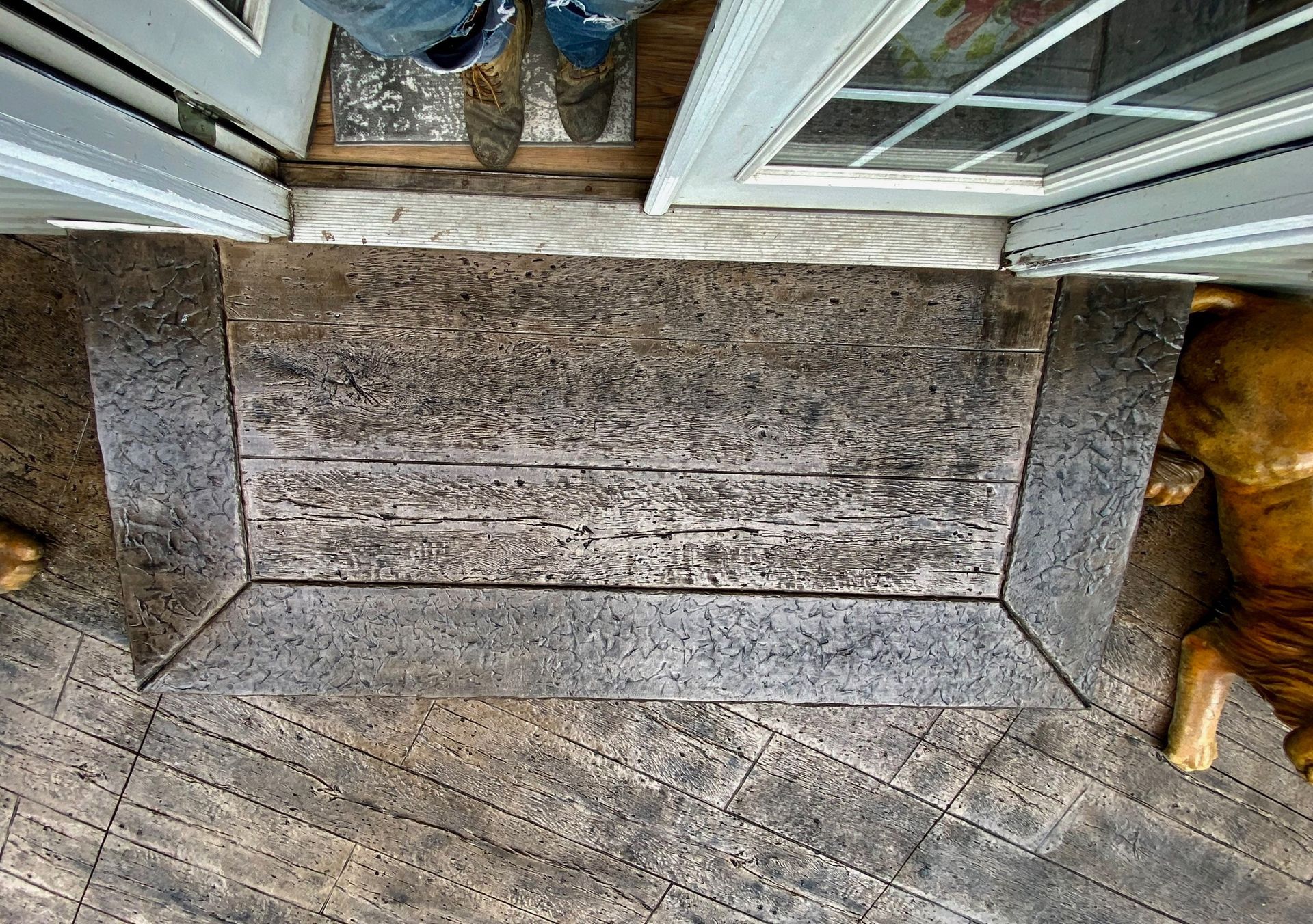 A weathered wooden-look concrete porch step and entrance area, framed by a gray border.