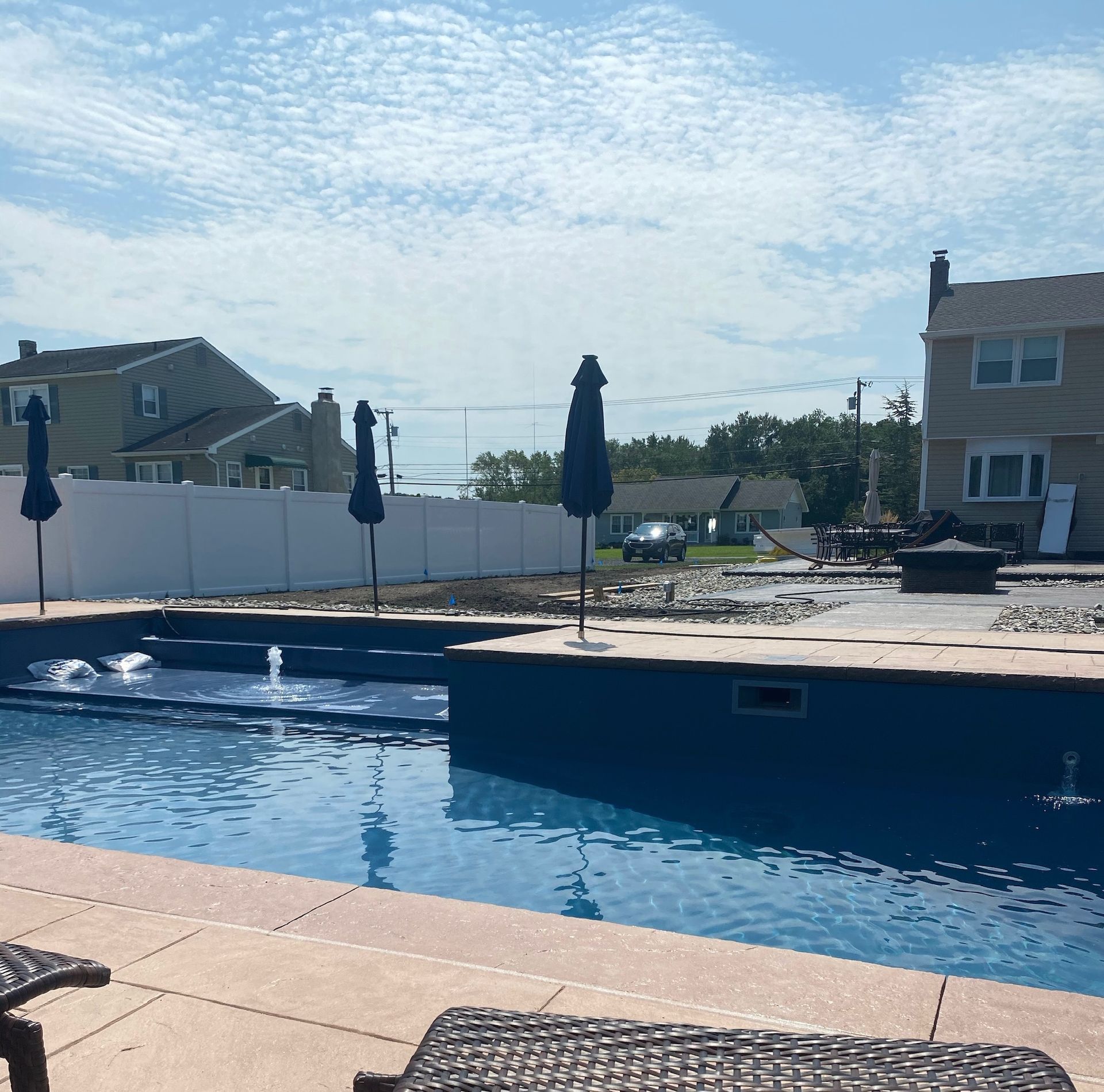 A backyard pool with umbrellas on a sunny day. Houses are visible in the background.