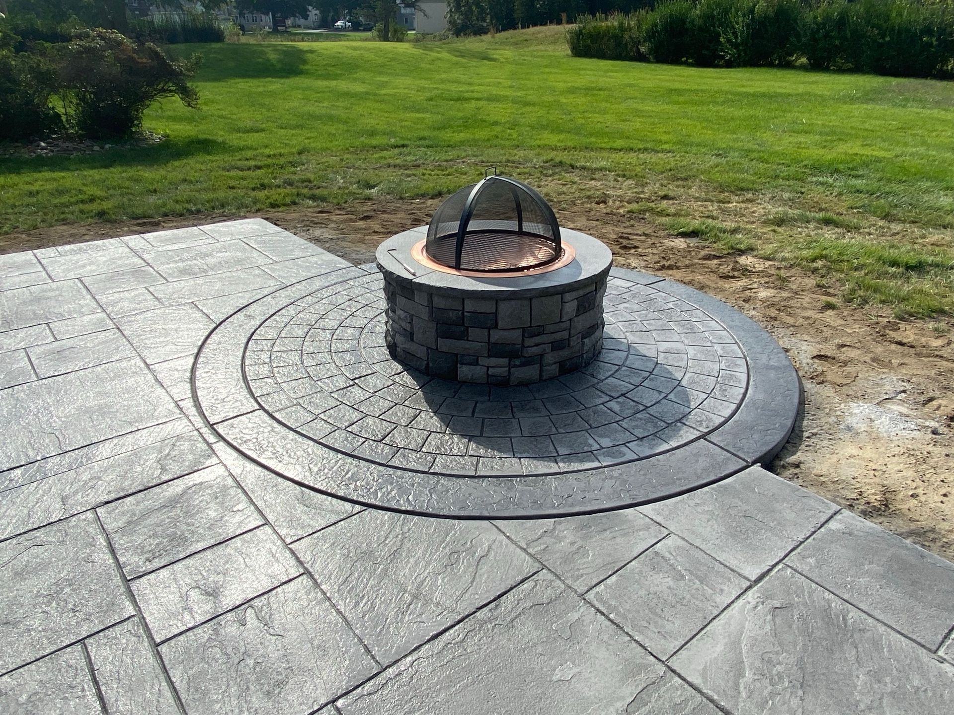 Gray patio with a fire pit, surrounded by green grass.