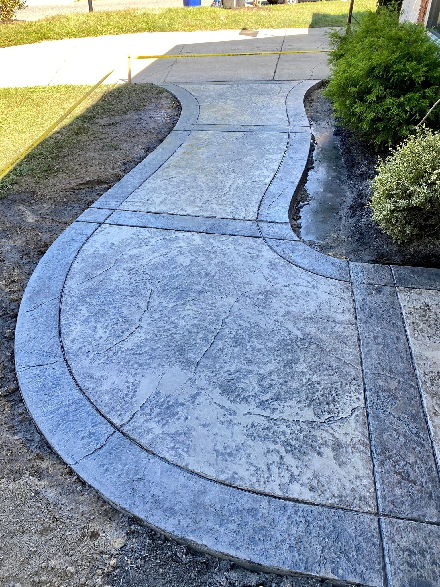 Concrete sidewalk with curved edges and textured surface, bordered by dark grey.
