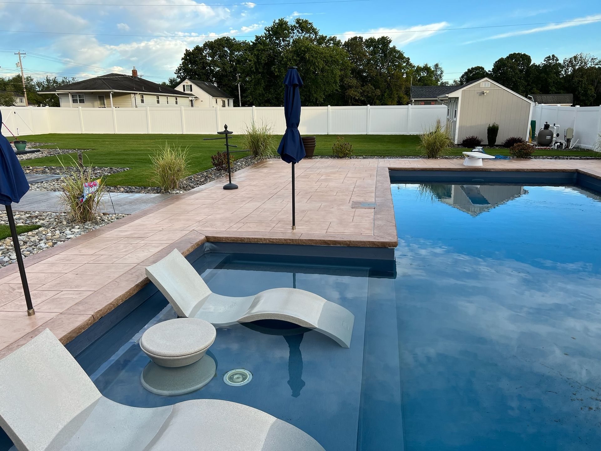 Poolside lounge area with chairs in the water and a blue umbrella.