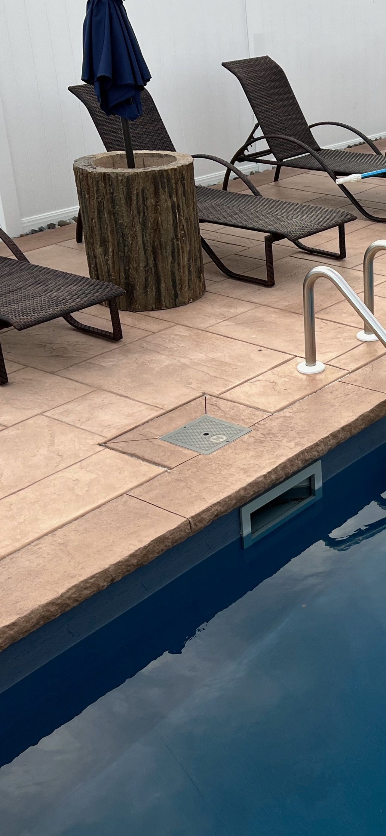 Poolside view with loungers, a tree stump table with an umbrella, and blue water.