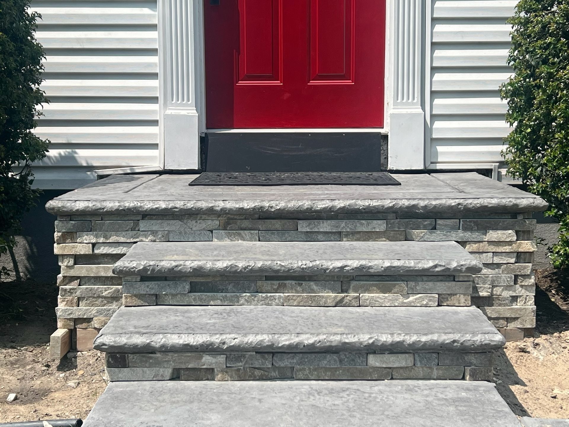 Gray stone steps leading up to a red door with white trim. The steps have stone accents.