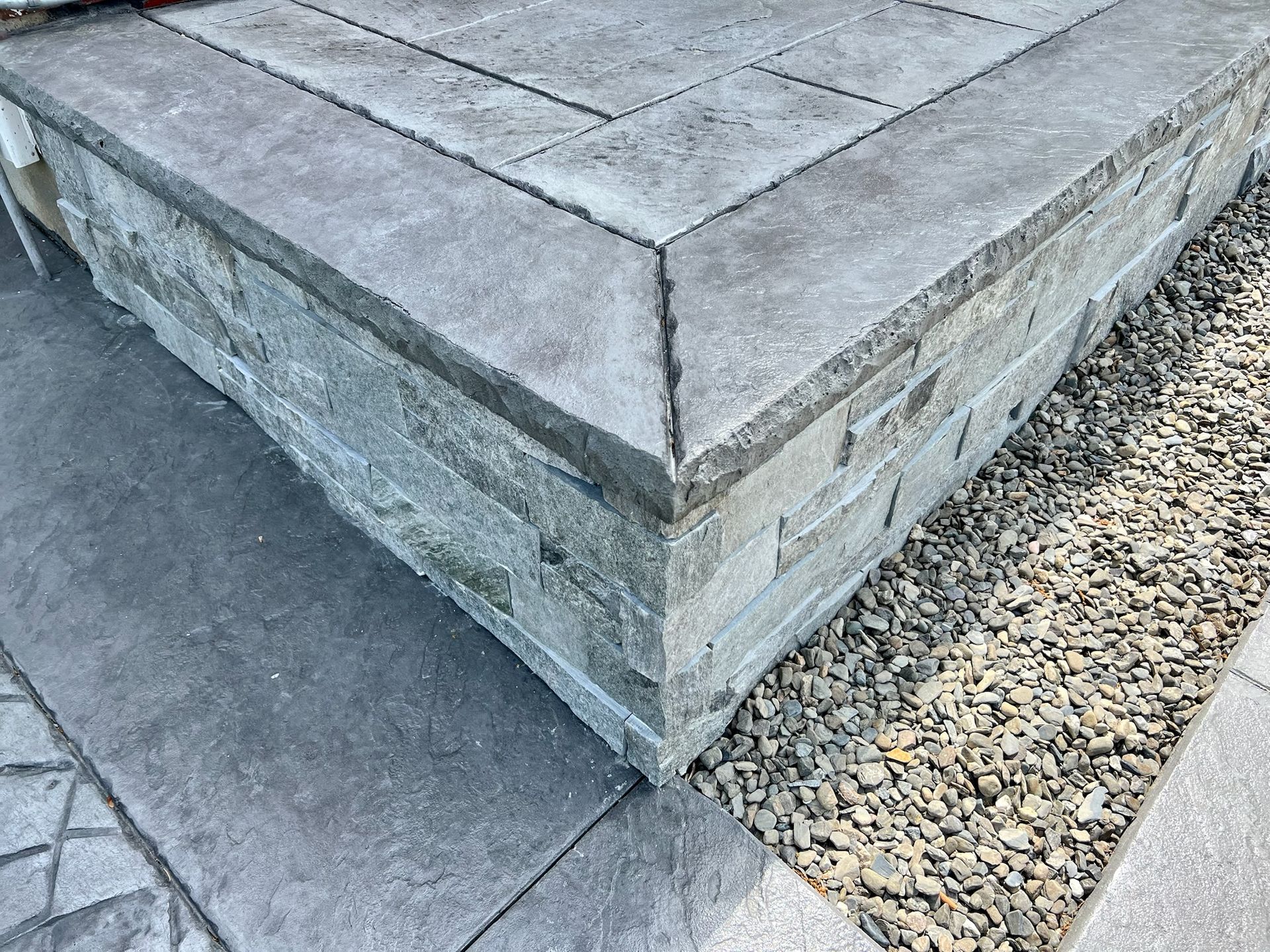 Stone steps with a gray facade and gravel edging.