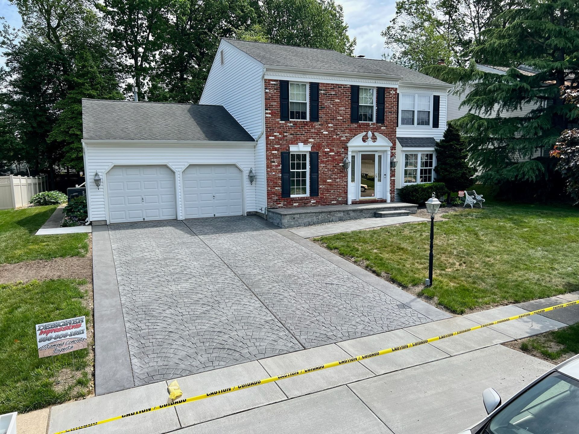 Two-story house with a newly paved gray driveway. Brick facade, white trim, garage, and lawn.