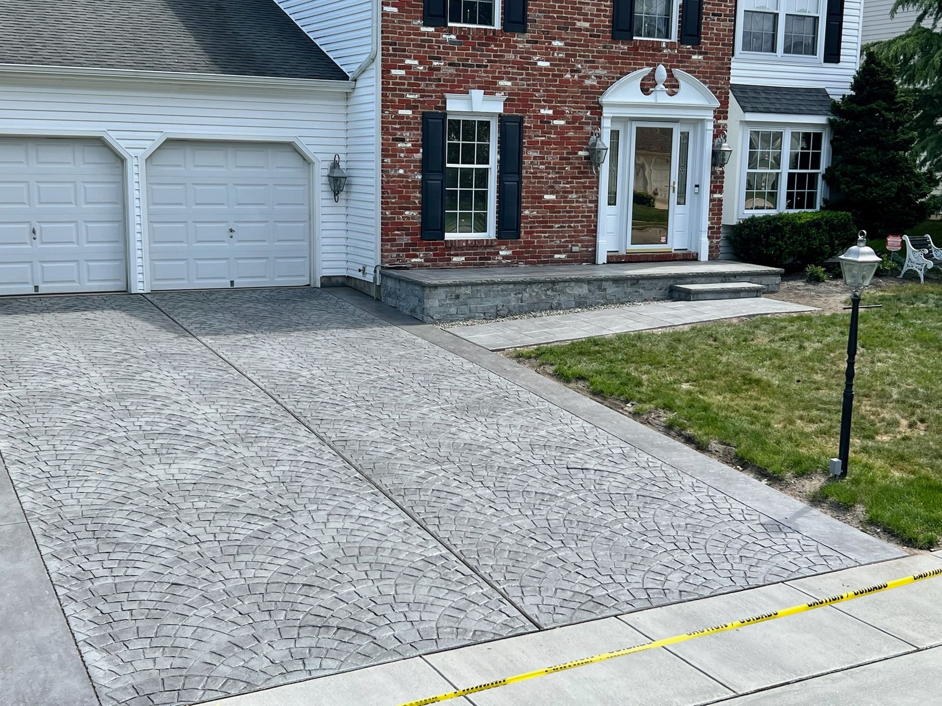 Gray patterned concrete driveway leading to a two-story brick house with white garage doors.