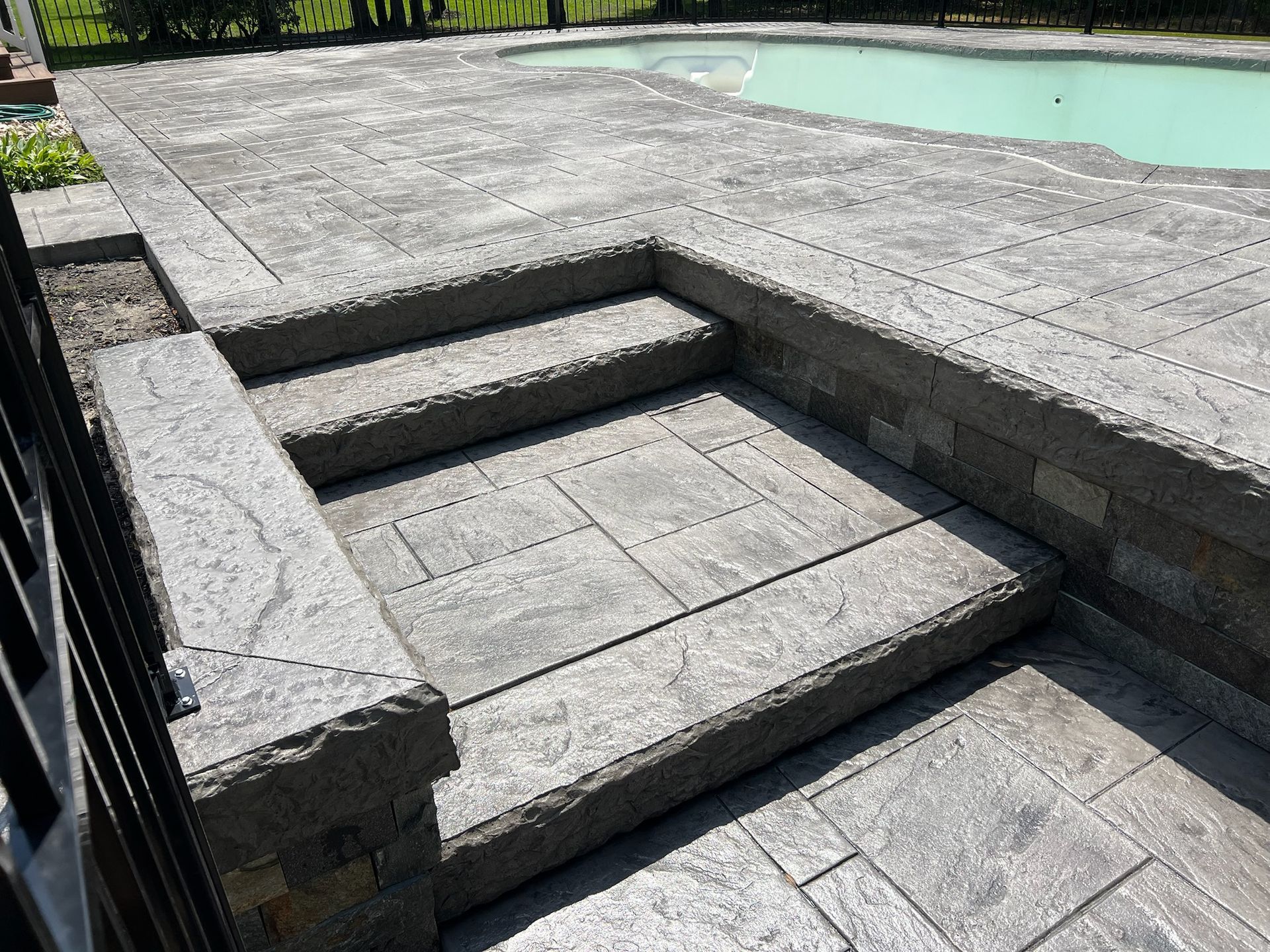 Gray stone steps leading down to a pool with a matching patio.