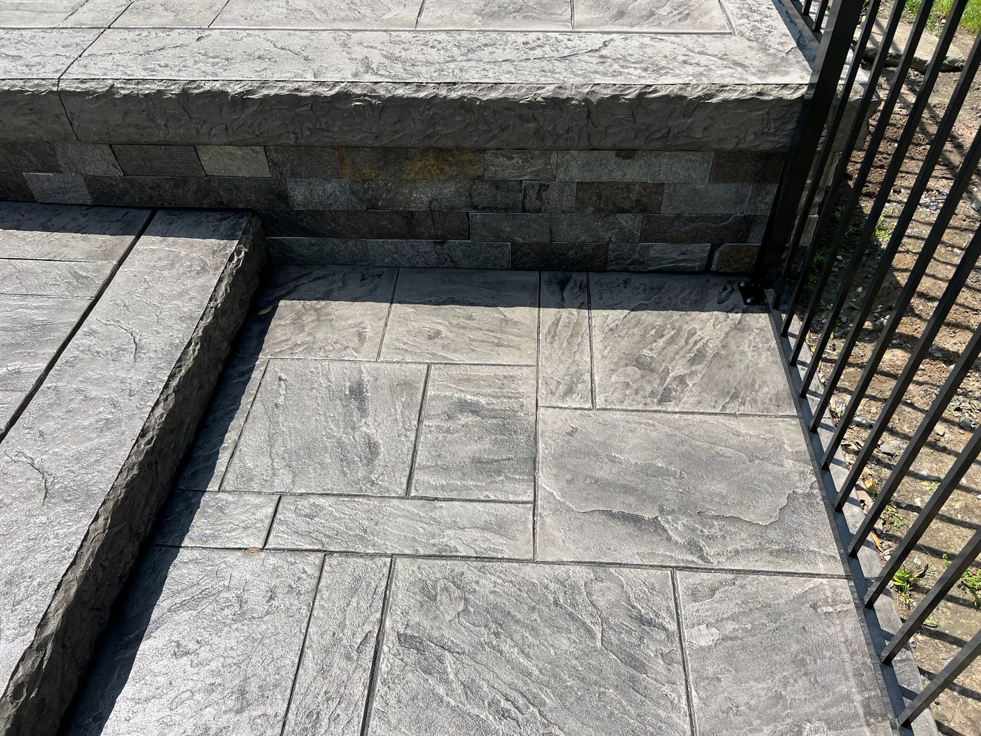 Gray stamped concrete patio with steps and a black metal fence.