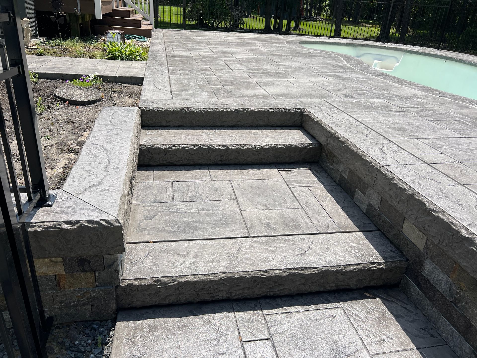 Stone steps leading to a pool patio. Gray stone, with a black metal fence on the left.