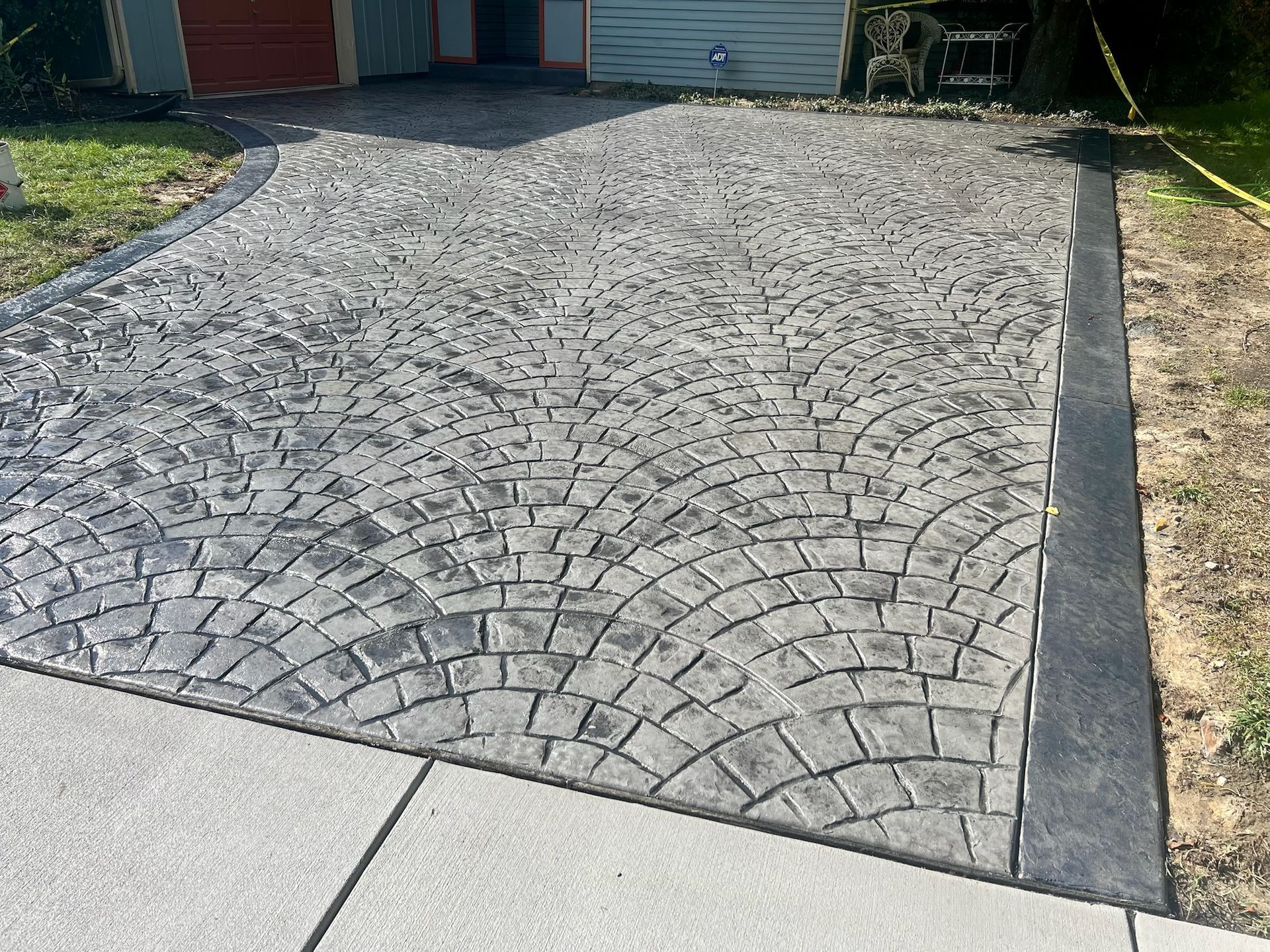 Gray, stamped concrete driveway with dark border and curved pattern.