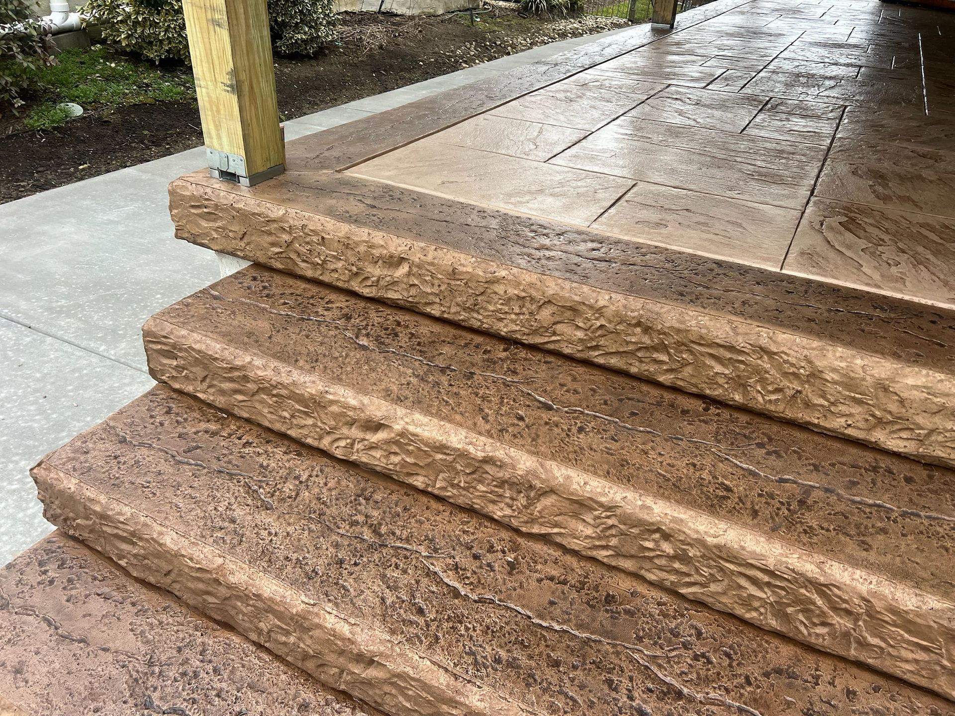 Brown textured concrete steps leading to a covered porch with similar concrete flooring.