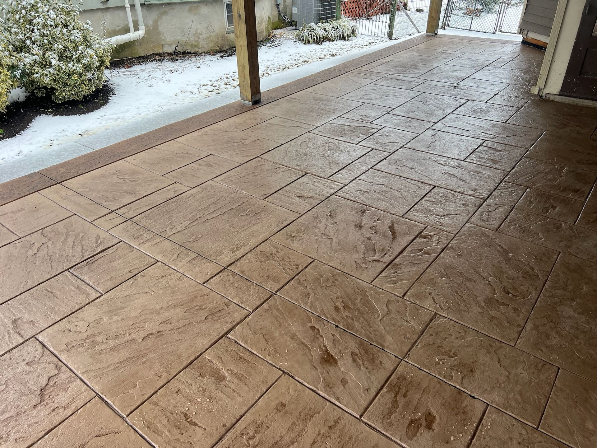Brown stamped concrete patio with snow, under a wooden overhang.