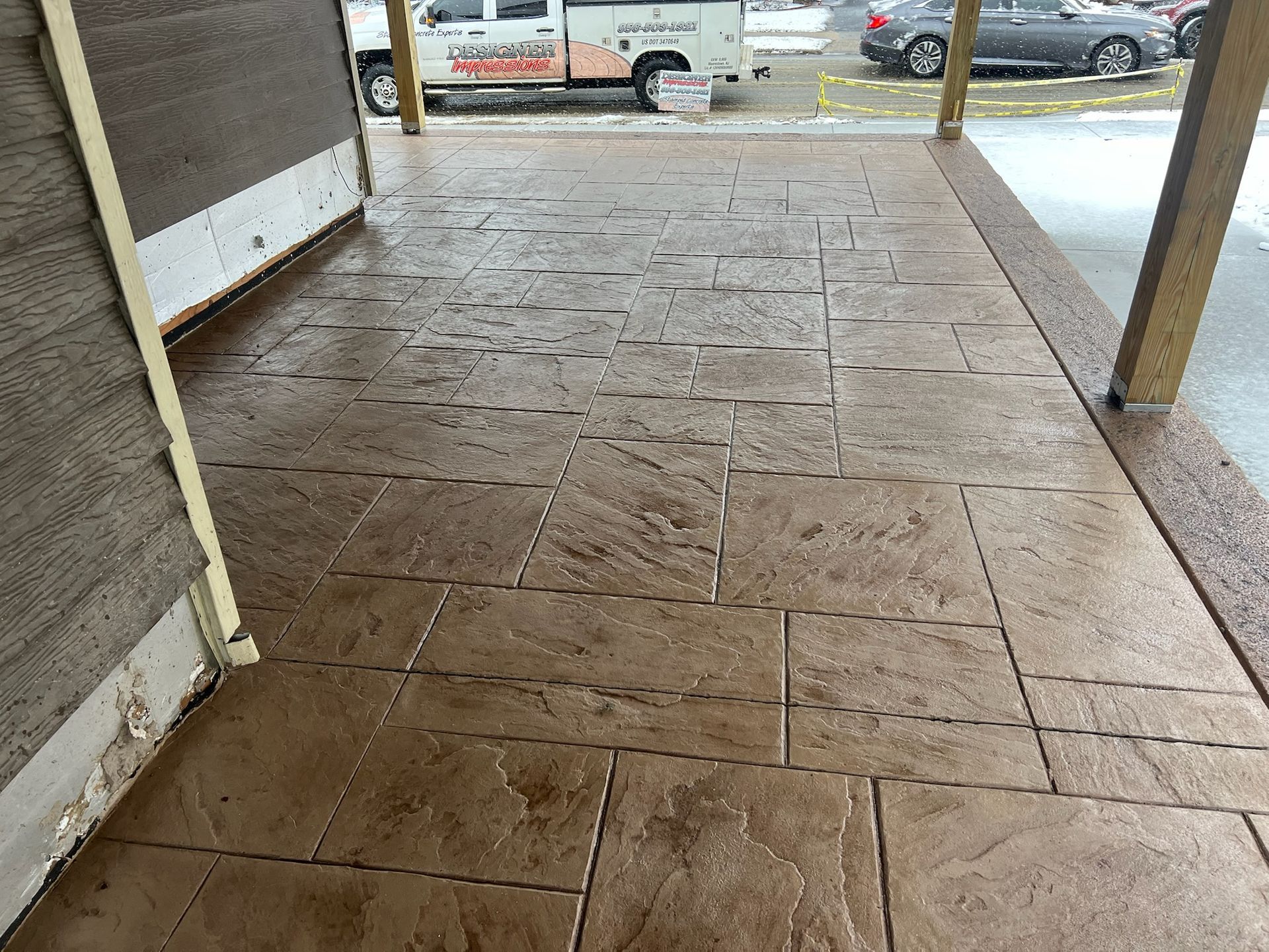 Brown, stamped concrete patio with a textured design. Wooden support beams frame the area.