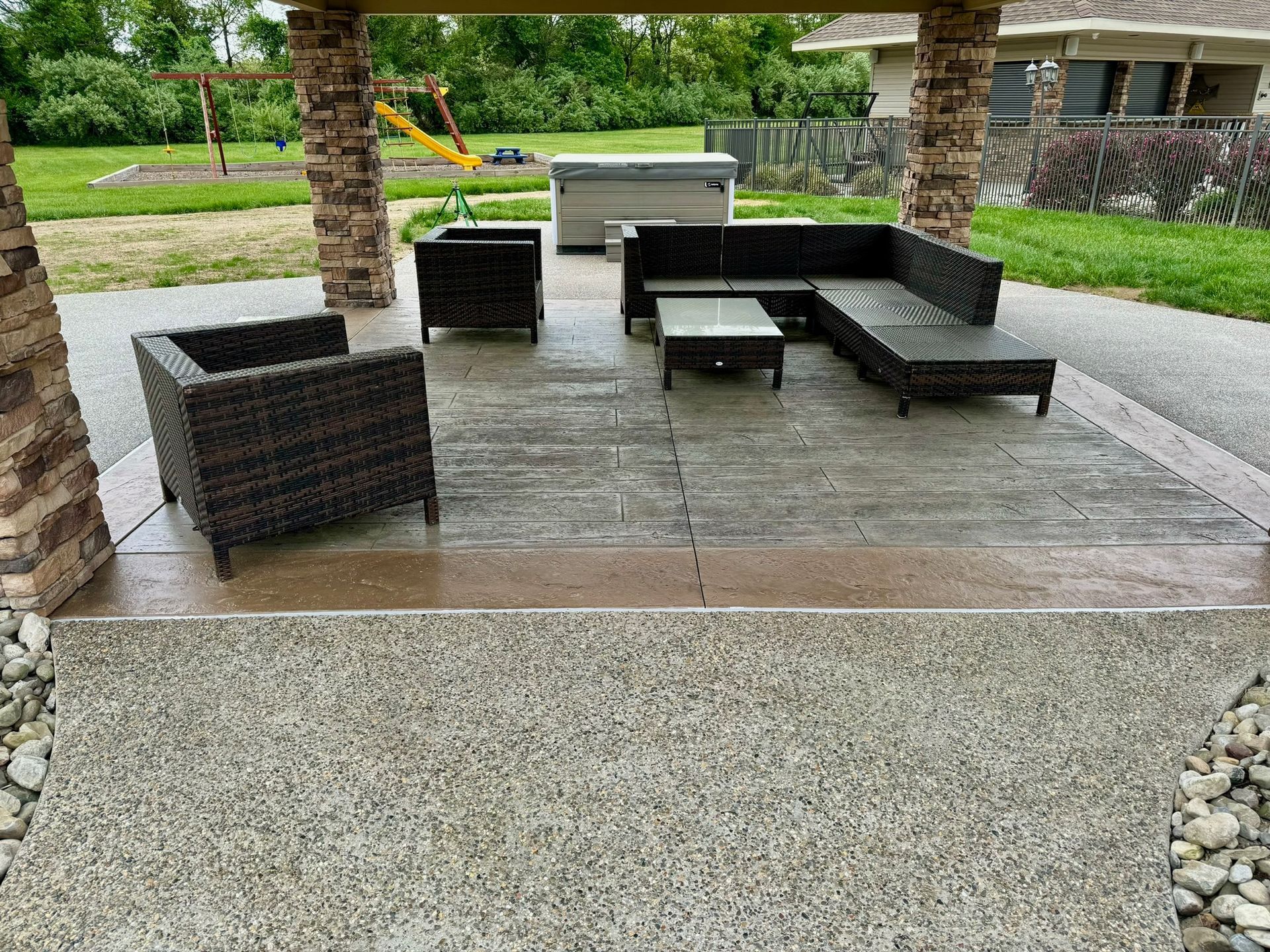 Patio with outdoor furniture, hot tub, and stone columns. Wet concrete in a backyard setting.