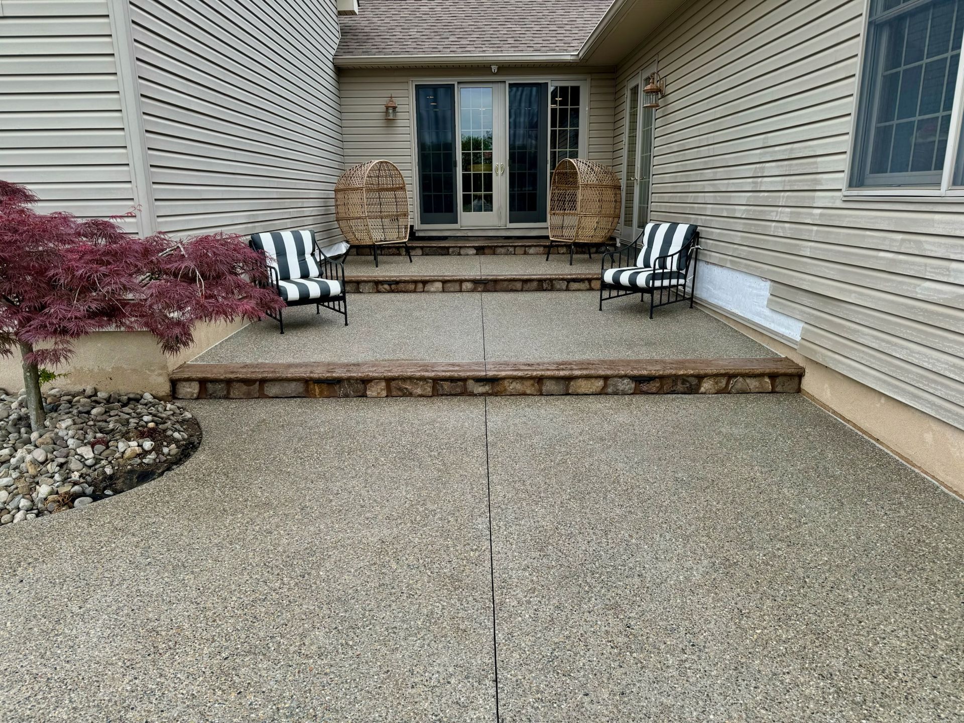 Patio with two steps leading to a house with two chairs. A tree is on the left.