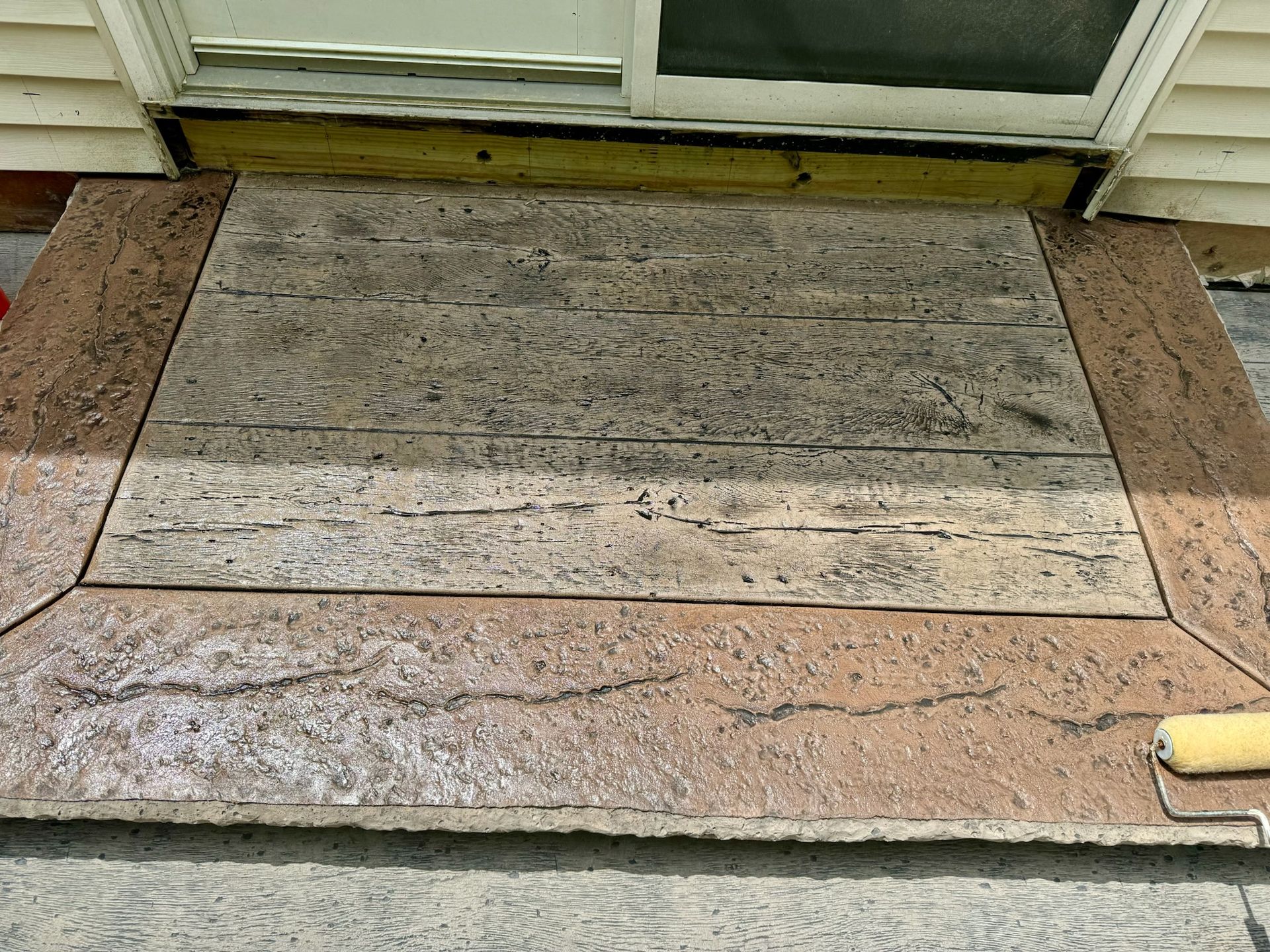 Stamped concrete step with wood and stone textures; bordered by brown stone.