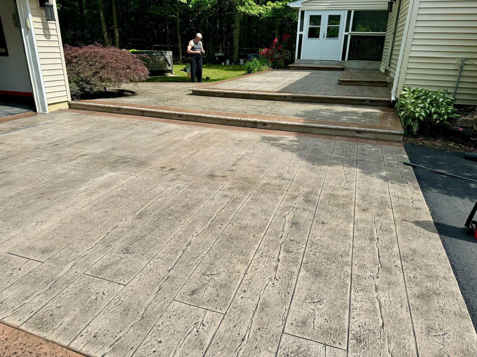 Stamped concrete driveway and patio with wooden steps, person standing near back door.