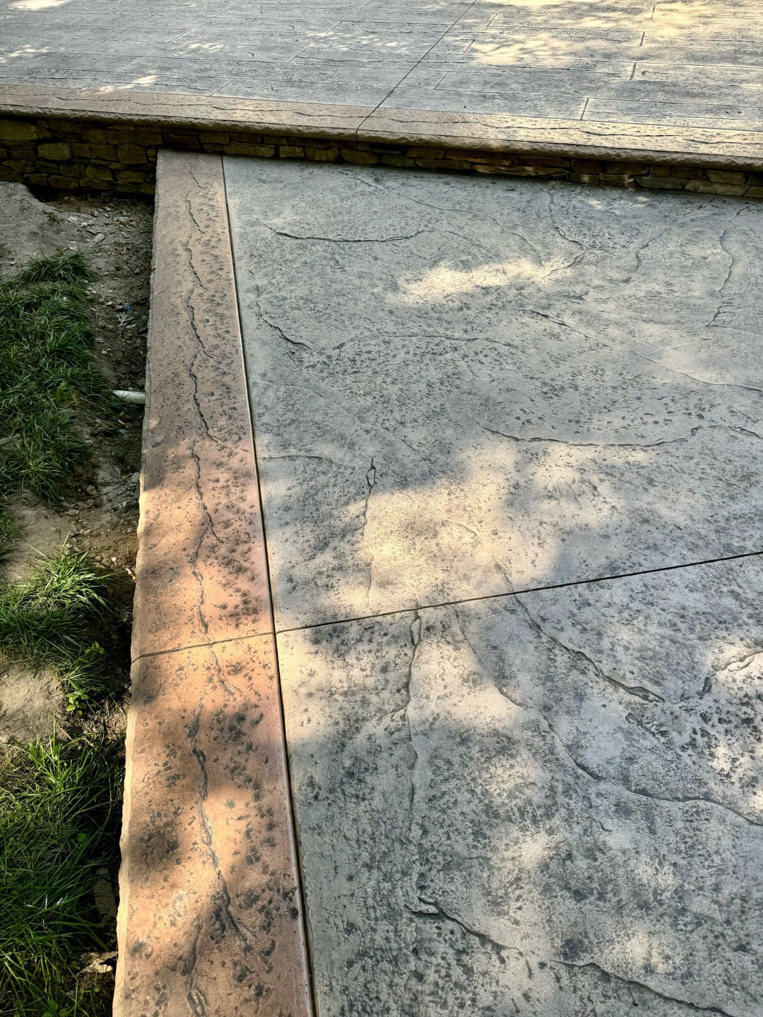 Concrete patio with a tan border next to grass and an adjacent concrete surface.