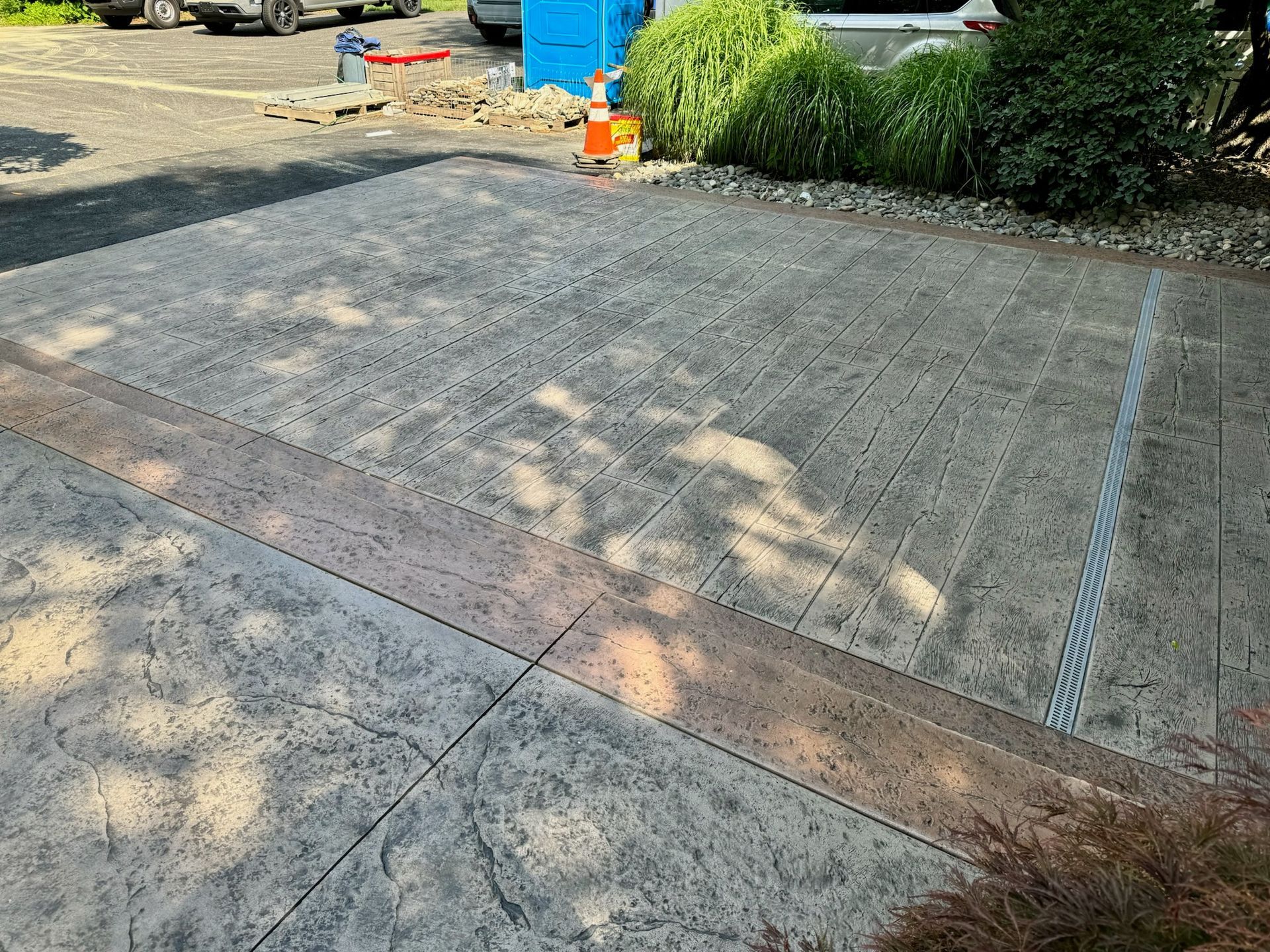 Driveway with stamped concrete and drainage, construction equipment nearby.