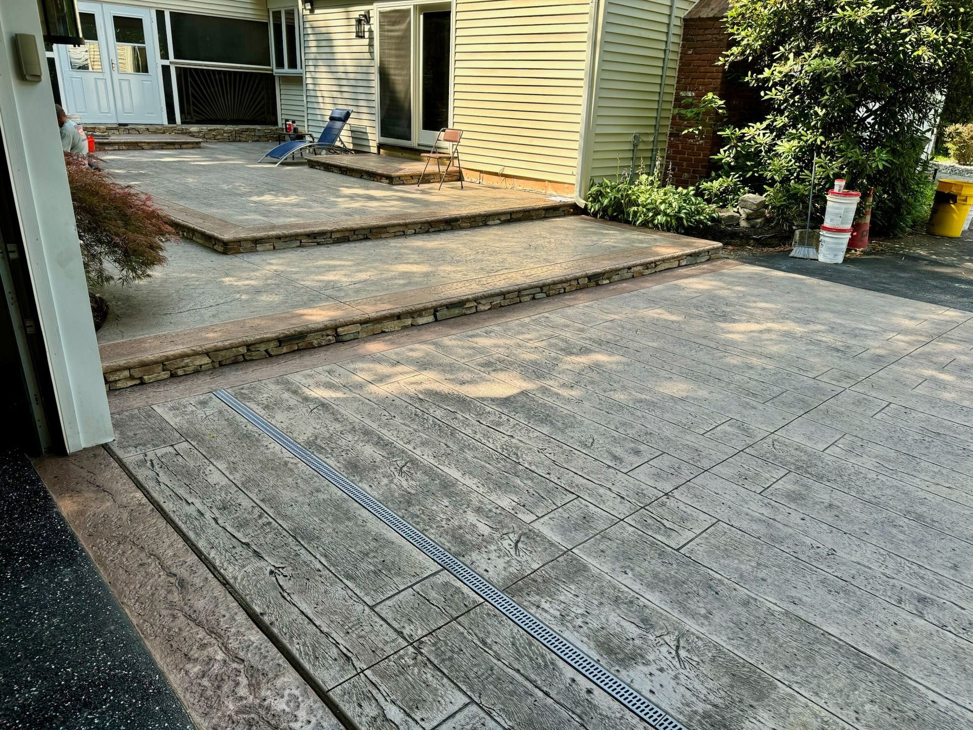 Concrete patio and steps, light gray, with a drainage channel. House exterior in the background.