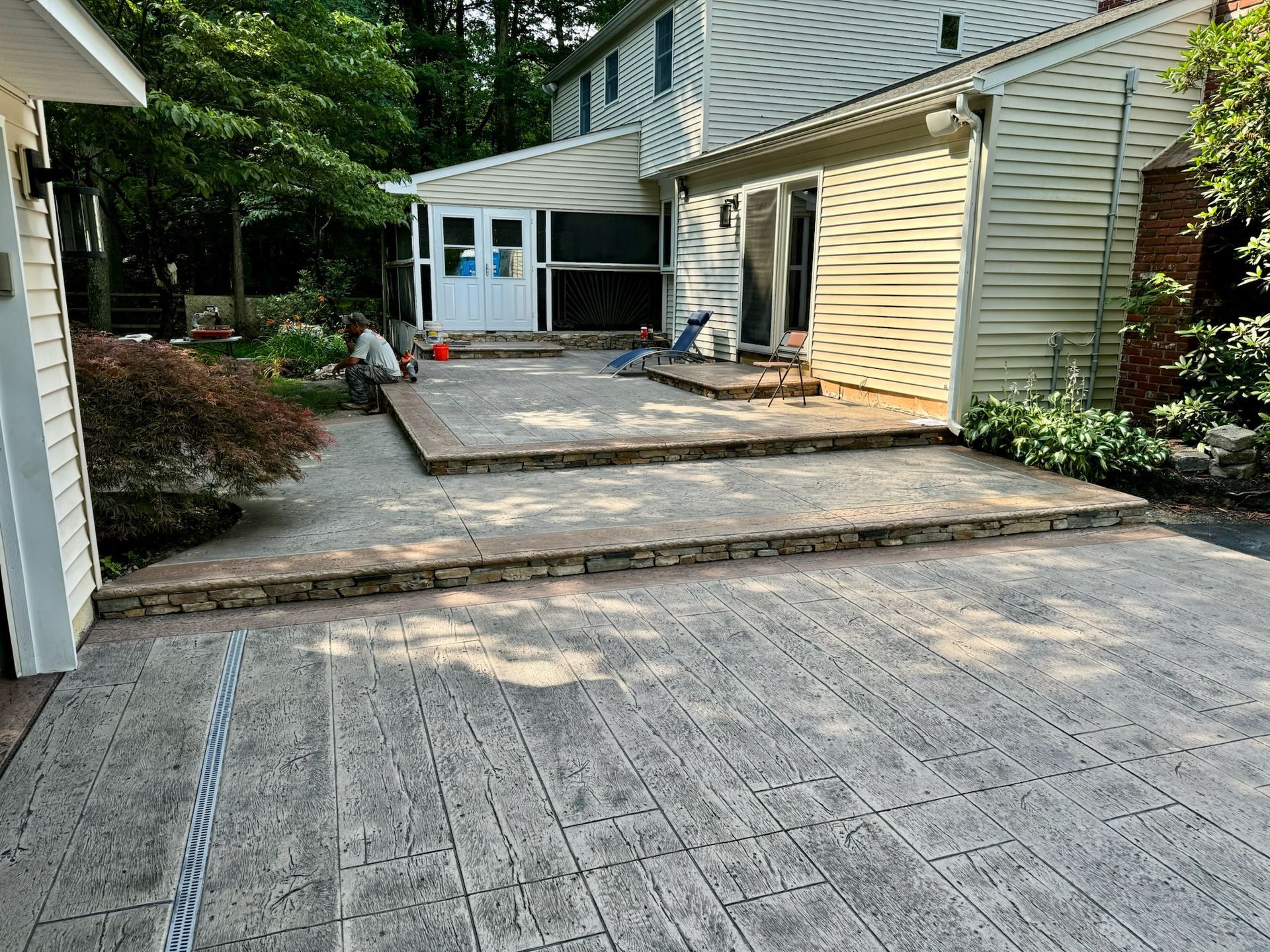 A two-tiered patio with stonework, leading to a house. The patio is grey and tan.