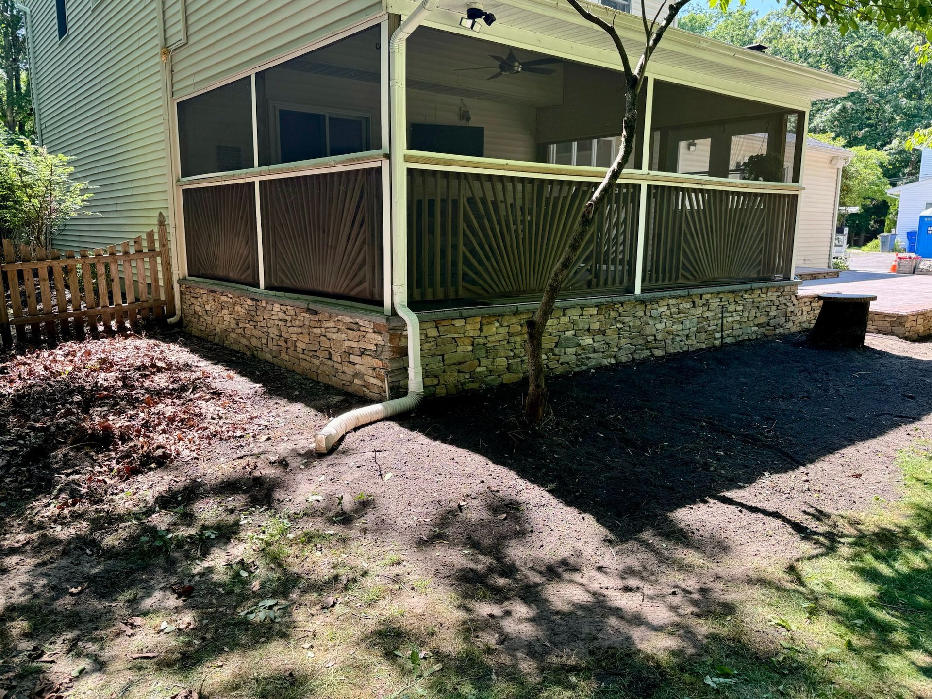 Screened-in porch with dark wood railing and stone base, surrounded by mulch and a small tree.