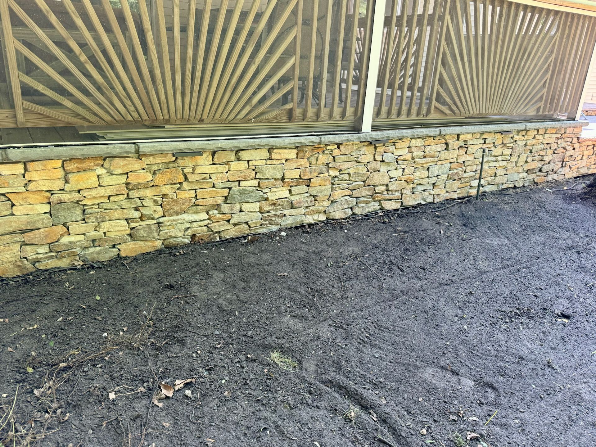 Stone wall with wooden beams above and dark gravel ground in the foreground.
