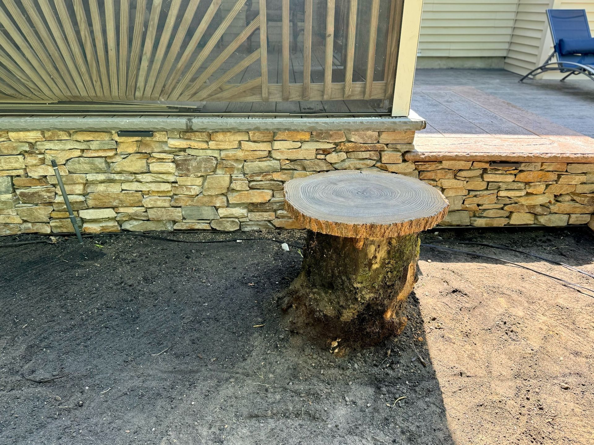 Stump table in front of stone wall next to a patio.