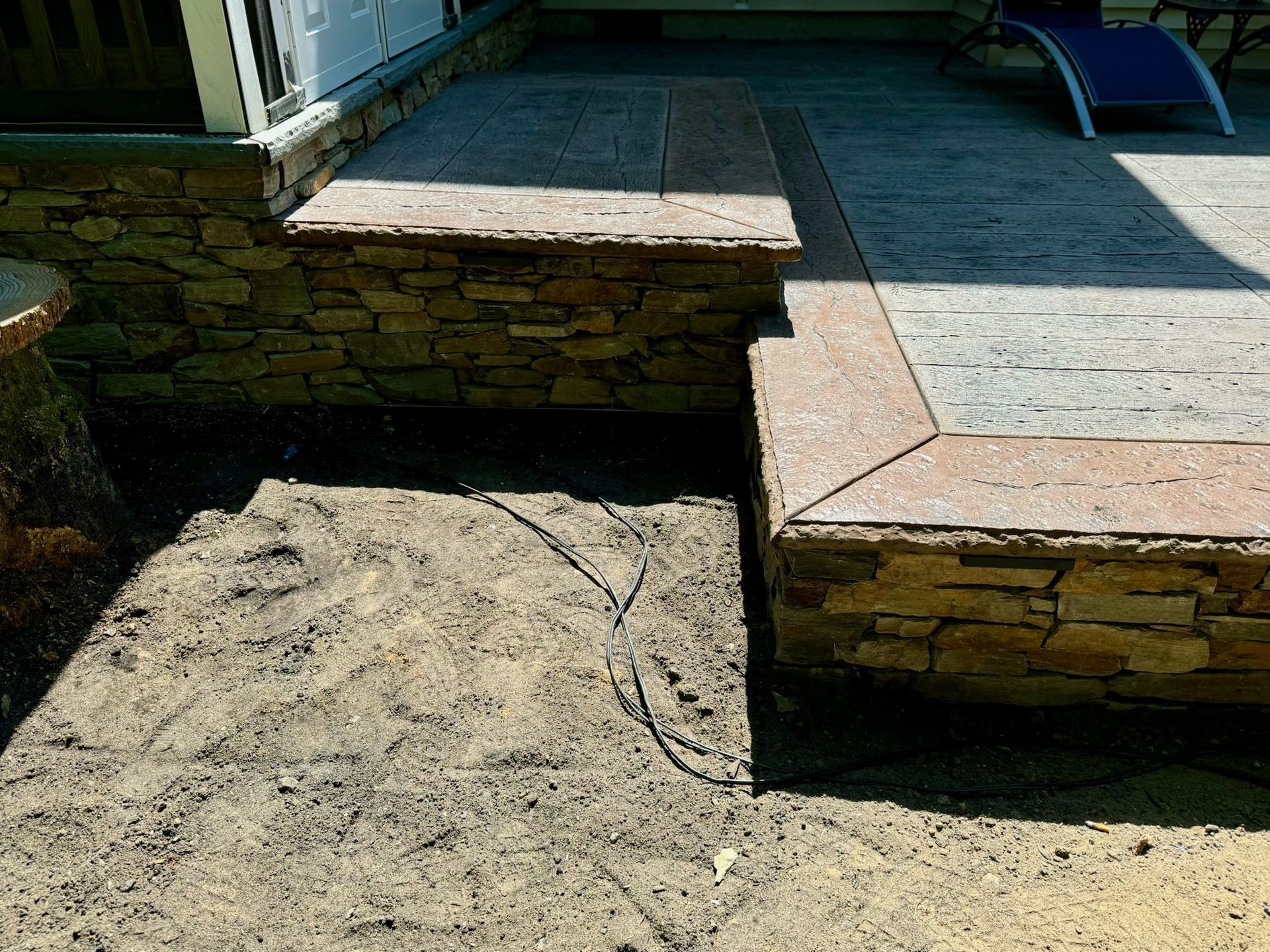 Stone patio with steps, bordering dirt. A ramp and chair are in the background.