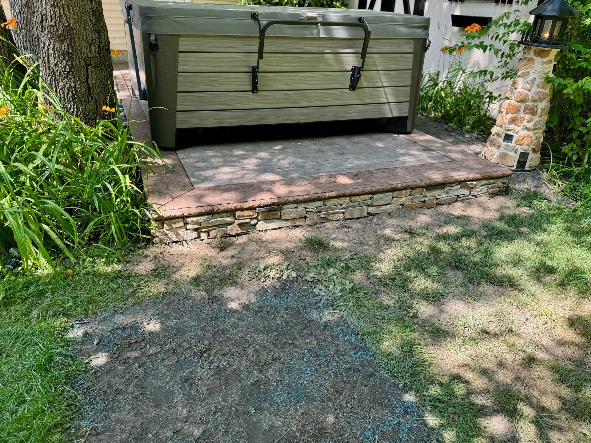 Hot tub on a stone patio, with grass and landscaping.