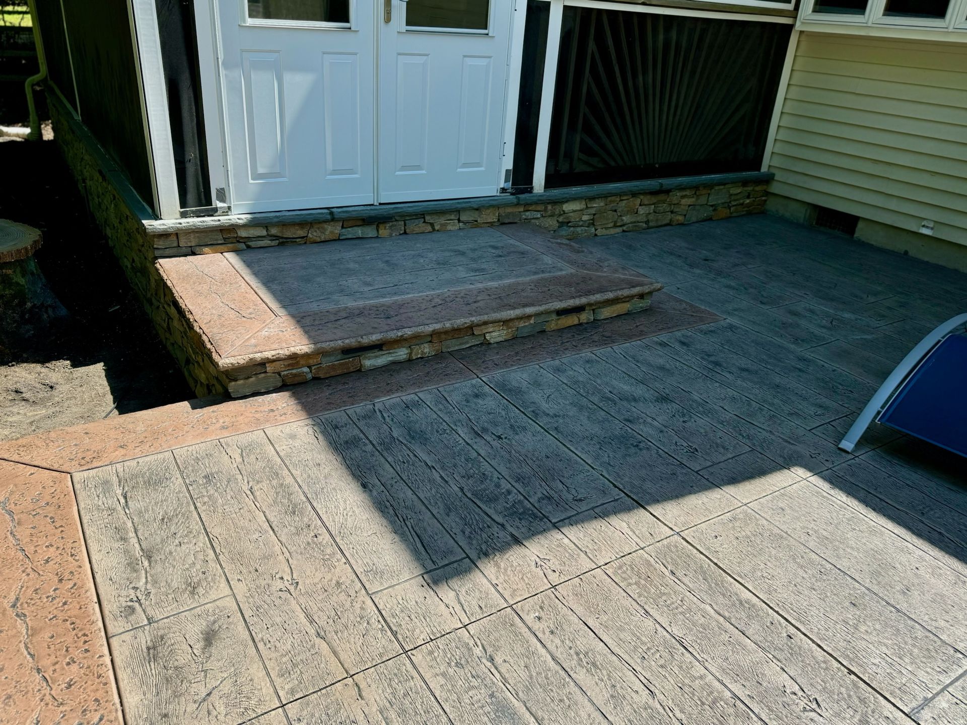 A concrete patio with steps leading to a doorway. Tan borders, grey textured surface.